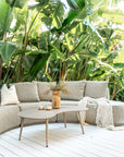 Laguna outdoor sofa in oat drift fabric with Solara coffee table on a sunlit deck surrounded by lush tropical greenery creating a relaxed resort style setting