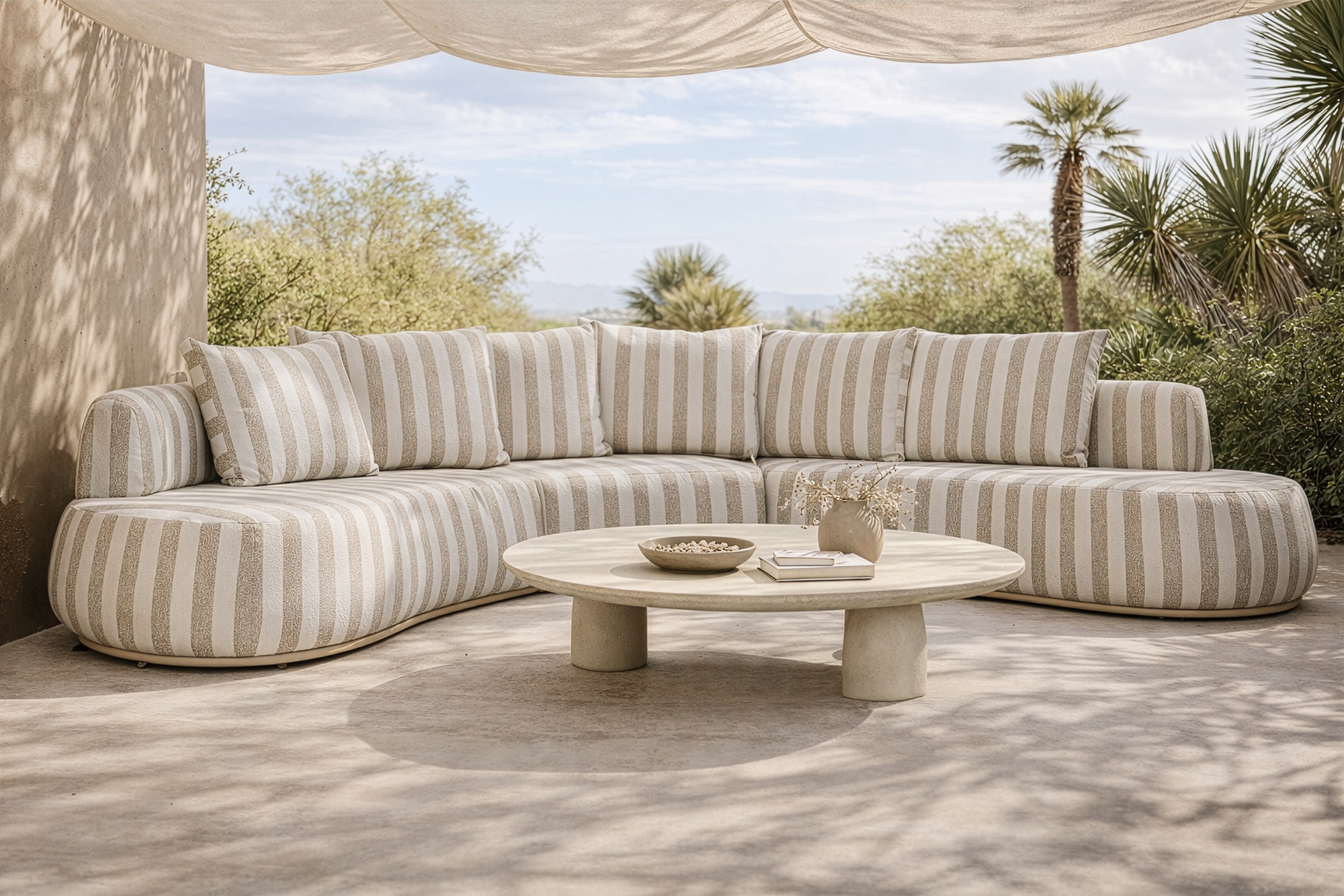 Laguna modular sofa in sand stripe fabric styled outdoors with a round coffee table in a relaxed natural setting.