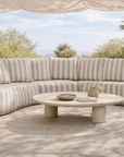 Laguna modular sofa in sand stripe fabric styled outdoors with a round coffee table in a relaxed natural setting.