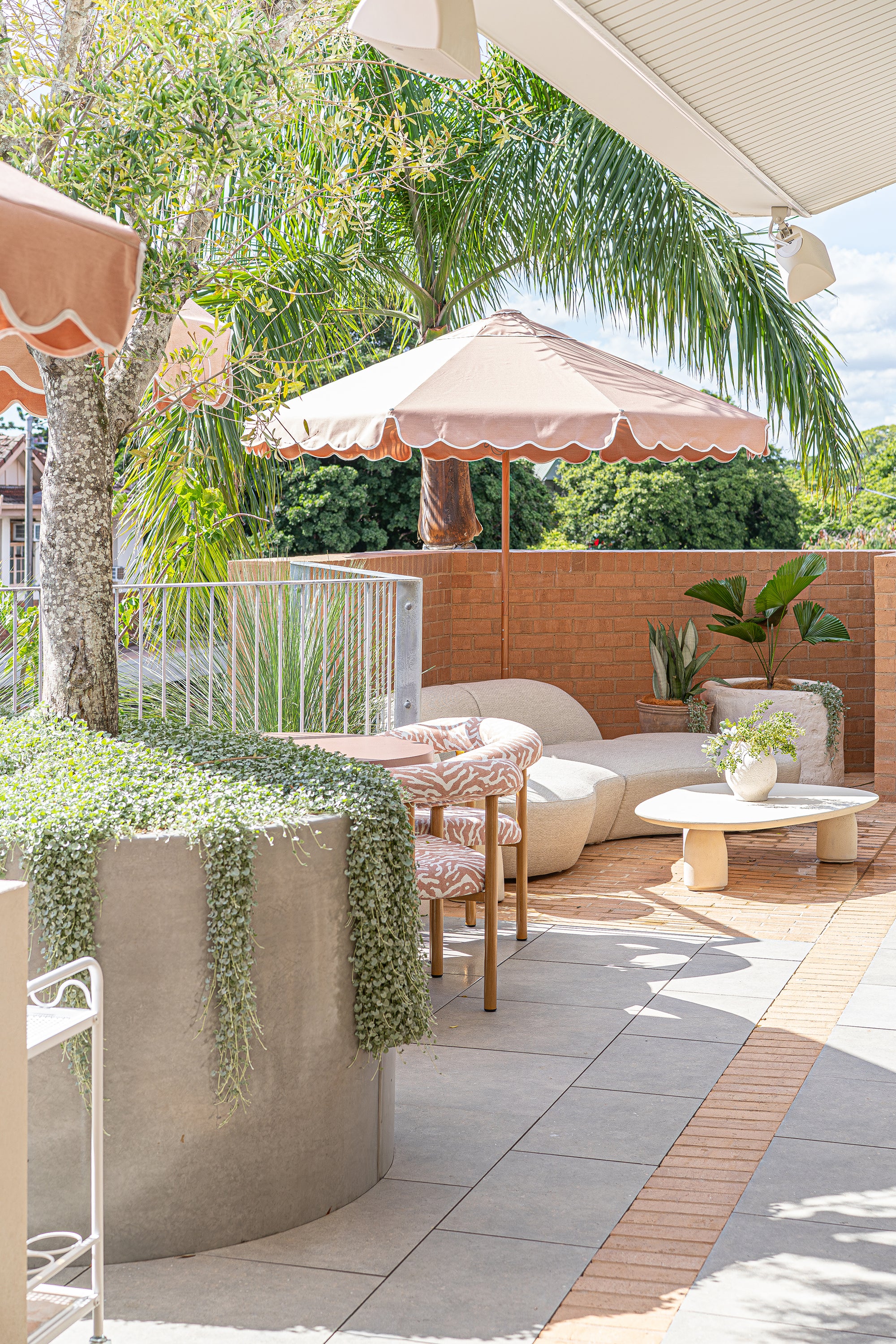 Lantara side table and large coffee table at Ruma rooftop bar styled with curved seating and umbrella creating a relaxed sunlit setting with natural textures.
