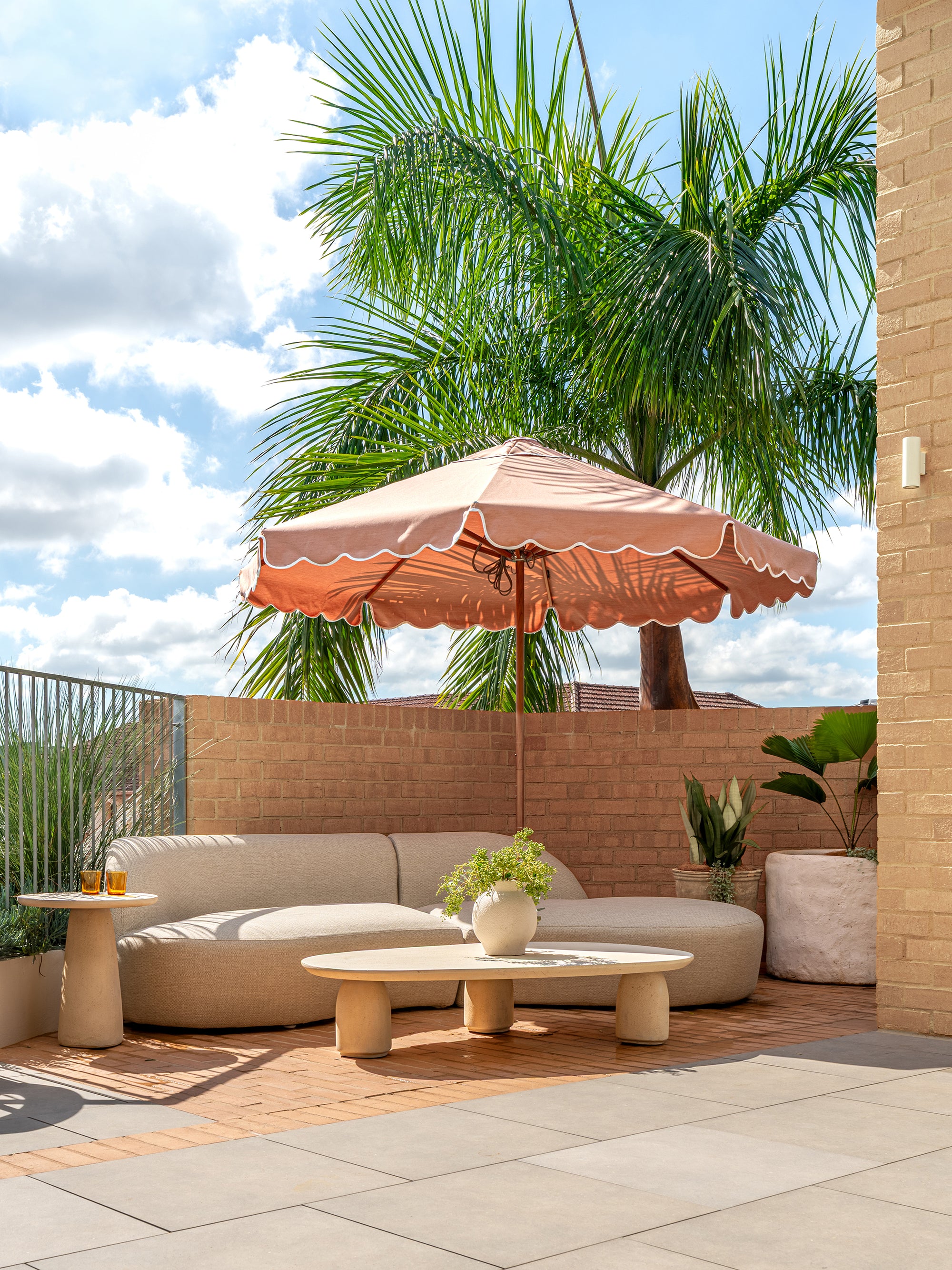 Lantara side table and large coffee table at Ruma rooftop bar styled with curved seating and umbrella creating a relaxed sunlit setting with natural textures.