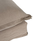 A plush linen slipcover ottoman in a warm taupe tone, featuring a relaxed silhouette with a soft cushion top. Perfect for versatile seating, a footrest, or as a stylish accent in contemporary and coastal-inspired interiors