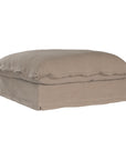 A plush linen slipcover ottoman in a warm taupe tone, featuring a relaxed silhouette with a soft cushion top. Perfect for versatile seating, a footrest, or as a stylish accent in contemporary and coastal-inspired interiors