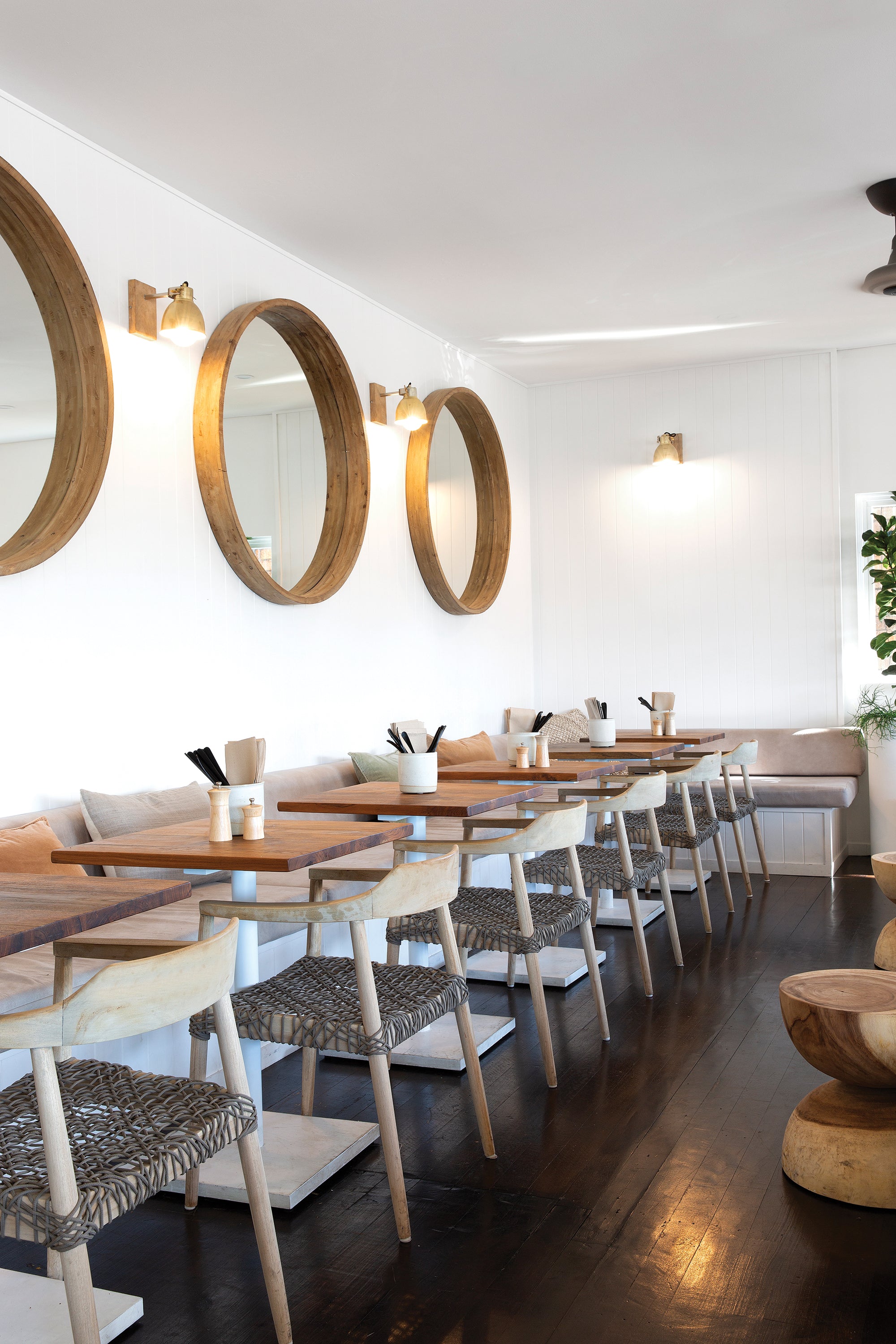Modern restaurant interior featuring wooden dining chairs with woven rope seats and natural wood tabletops, creating a relaxed coastal ambiance