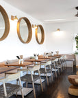 Modern restaurant interior featuring wooden dining chairs with woven rope seats and natural wood tabletops, creating a relaxed coastal ambiance