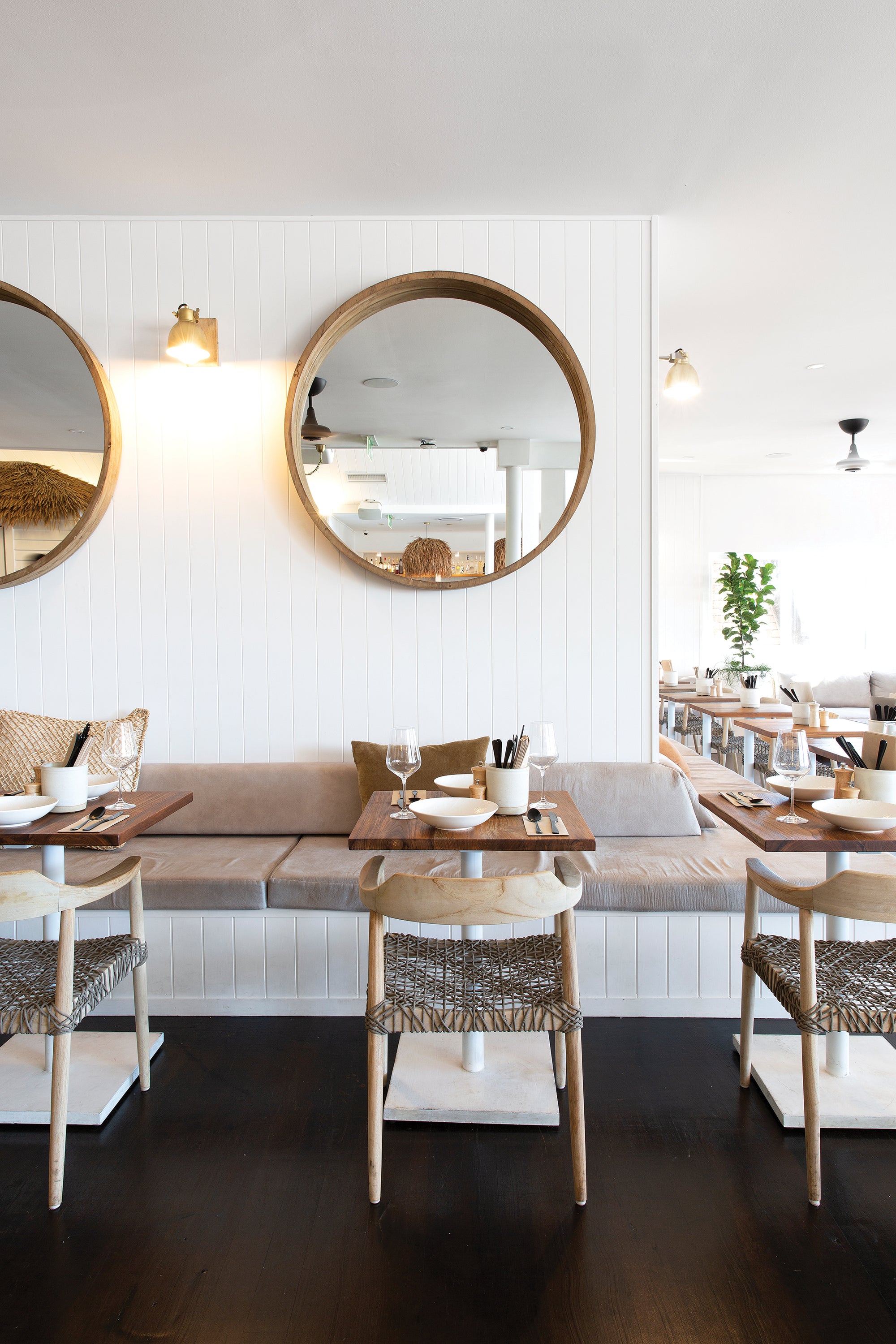 Modern restaurant interior featuring wooden dining chairs with woven rope seats and natural wood tabletops, creating a relaxed coastal ambiance