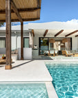 Luxury outdoor poolside lounge with rattan hanging chair, timber pergola, cushioned built-in seating and dining space overlooking the pool.