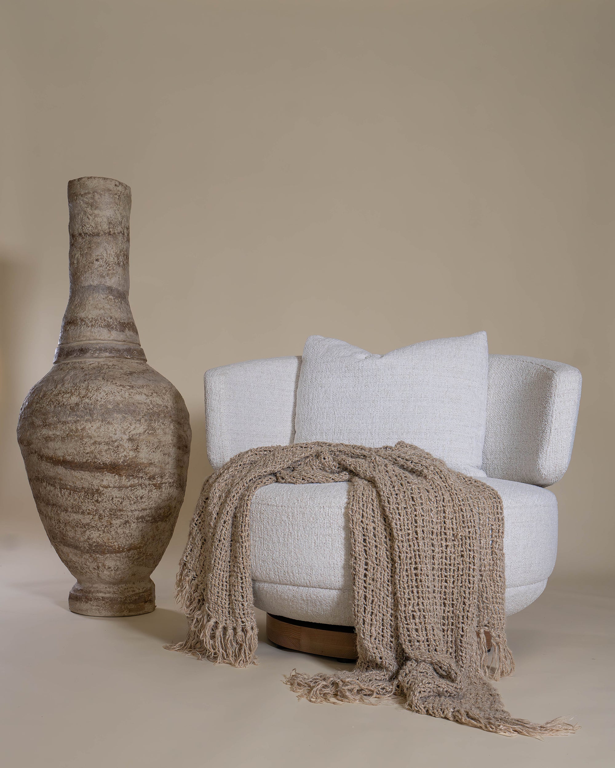 The Maja Occasional Chair from Kulala Living, elegantly styled with a textured throw and cushion, featuring a boucle swivel design and a curved backrest for a cosy and sophisticated interior setting