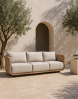 Malusi Sofa three-seater in natural wicker with neutral cushions, styled in a sunlit Mediterranean-inspired courtyard with olive trees