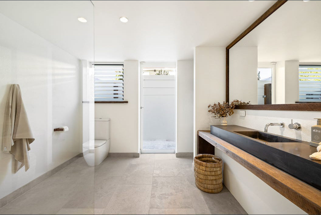 Mara basket in natural handwoven finish styled beneath a timber bathroom vanity with stone flooring and soft neutral interior tones