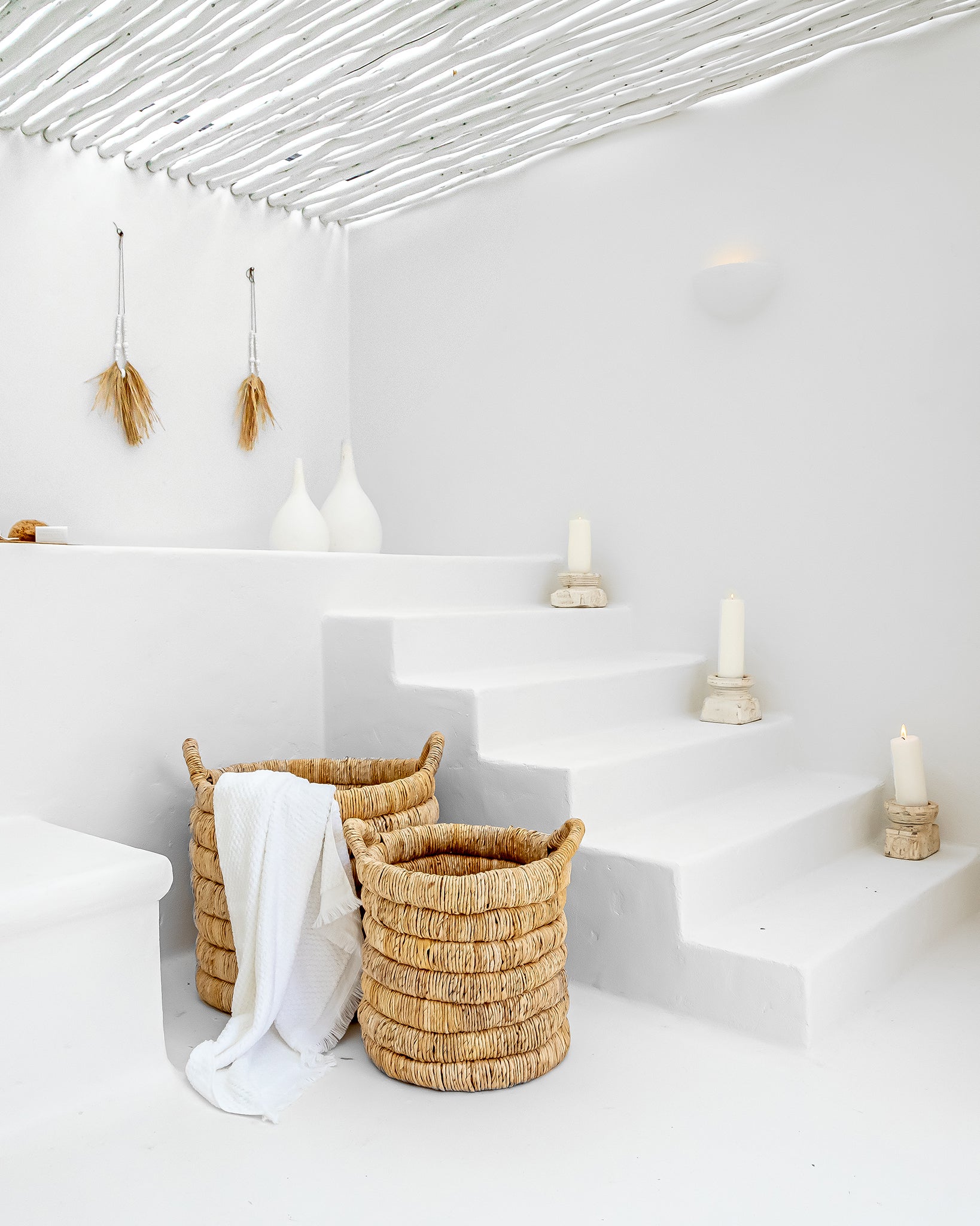 Mara natural handwoven storage baskets styled on white plaster steps with candles and soft minimal decor