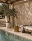 Natural Meera stool crafted from magnesium oxide styled beside a poolside daybed creating a warm organic retreat with rustic character and natural textures.