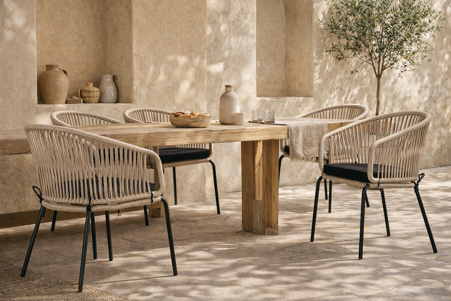 Melela armchair in black and natural rattan styled around a timber dining table in a sun dappled mediterranean inspired courtyard setting