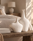 KULALA Living Meraki whitewashed fibre cement vases styled on a rustic timber bench in a warm neutral bedroom.