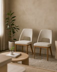 Pair of mid-century inspired dining chairs with cream upholstery and natural oak legs, styled in a minimalist living space with soft neutral tones