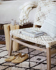 Light-filled modern boho bedroom with a wooden bed, layered neutral bedding, woven accent chair with white rope weave, natural wood side tables, and organic decor accents.