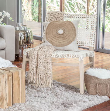Light-filled modern boho livingroom with layered neutral throws, woven accent chair with white rope weave, natural wood side tables, and organic decor accents.