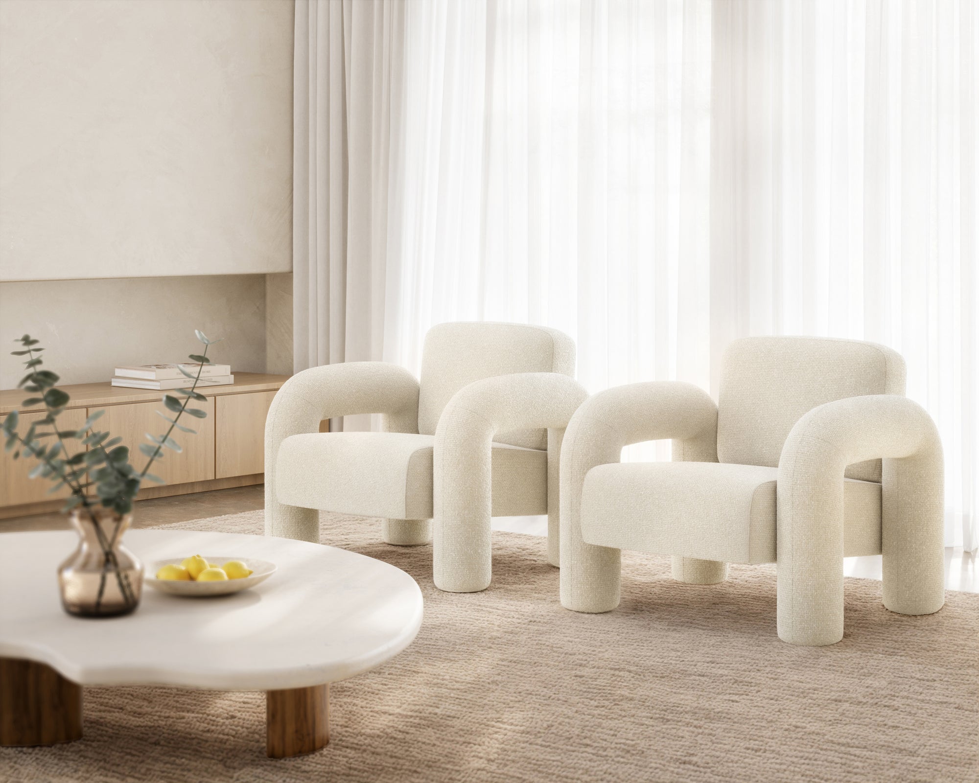A pair of modern boucle armchairs with sculptural rounded arms, upholstered in soft white fabric, styled in a serene contemporary lounge setting with natural tones
