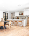 A beautifully styled modern coastal kitchen featuring a spacious island with wooden bar stools, natural timber flooring, white cabinetry, and a black dining table with matching wooden chairs, creating a warm and inviting space
