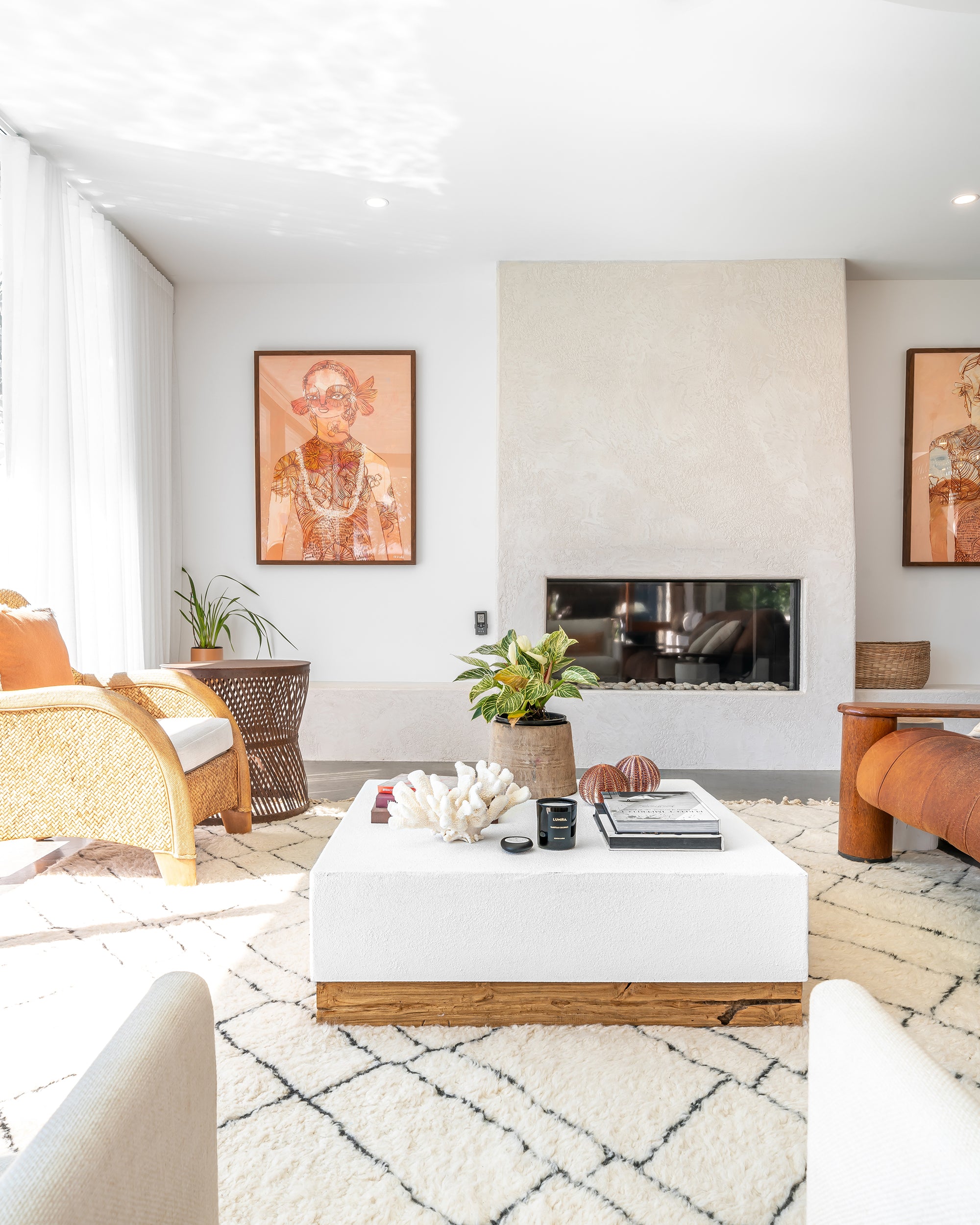 A beautifully styled modern coastal living room featuring a white and wood coffee table, textured neutral decor, and a built-in fireplace. The space is accented with woven and rattan furniture, tribal artwork, and soft natural light, creating a warm and inviting atmosphere
