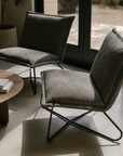 Modern lounge chair with charcoal upholstered cushions and black metal frame styled in a sunlit contemporary living space.