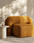 A luxurious mustard velvet lounge chair with a sculptural, curved backrest and a matching ottoman, offering a bold yet elegant statement piece for contemporary interiors