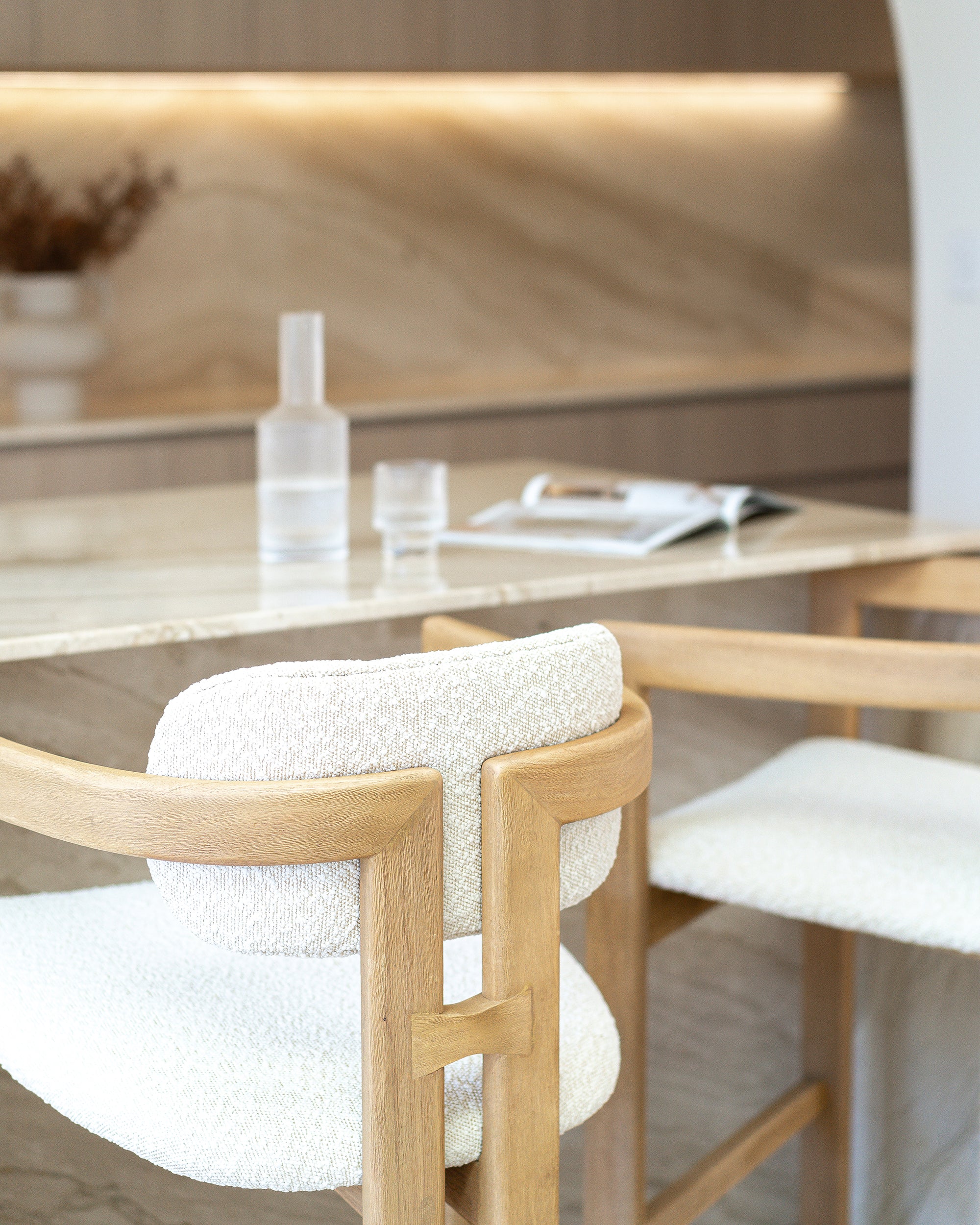 Rubberwood counter-height chair with curved frame and ivory boucle upholstery, styled at a travertine kitchen island with soft neutral tones and minimal decor.