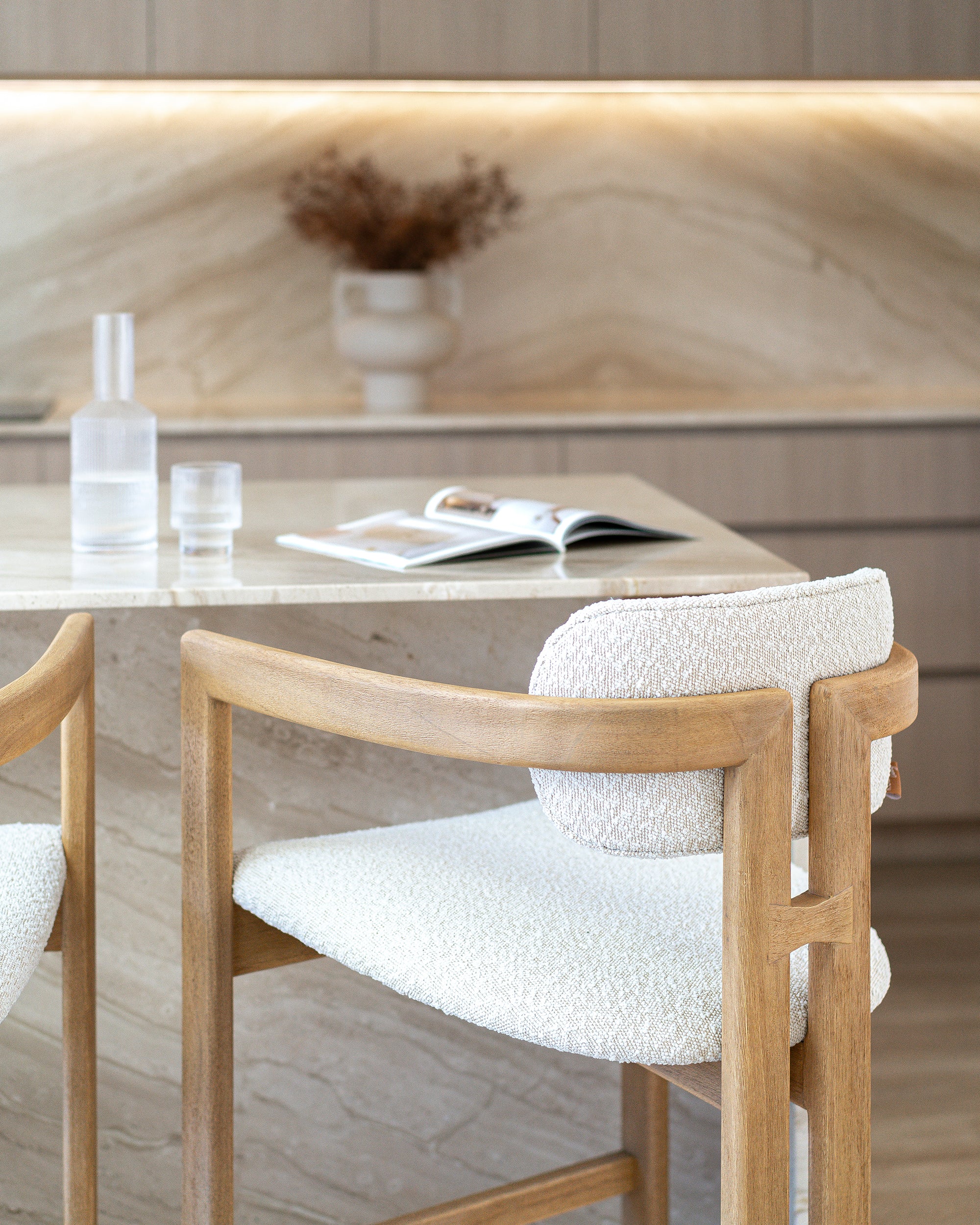 Rubberwood counter-height chair with curved frame and ivory boucle upholstery, styled at a travertine kitchen island with soft neutral tones and minimal decor.