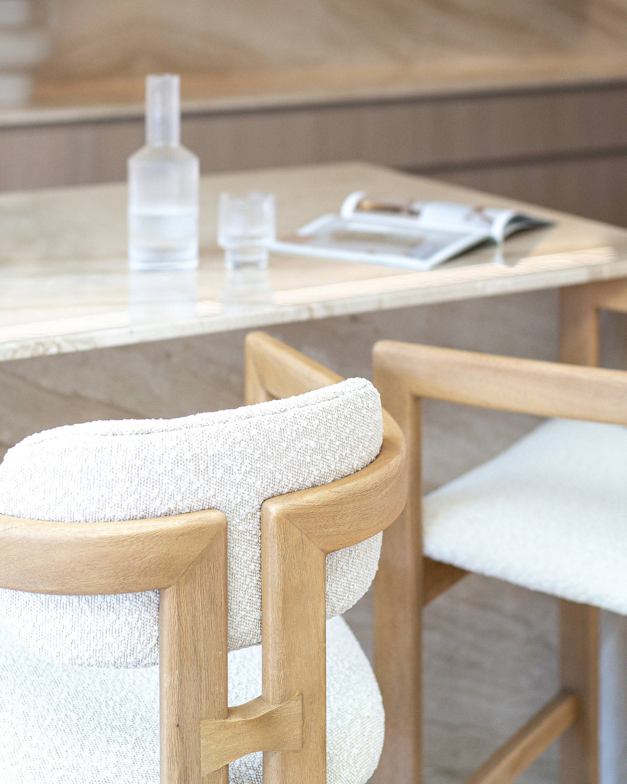 Rubberwood counter-height chair with curved frame and ivory boucle upholstery, styled at a travertine kitchen island with soft neutral tones and minimal decor.