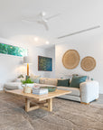 Modern lounge room with a natural aesthetic, featuring a neutral modular sofa with green cushions, a wooden coffee table with decor accents, woven wall hangings, and a textured floor rug