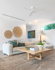 Modern lounge room with a natural aesthetic, featuring a neutral modular sofa with green cushions, a wooden coffee table with decor accents, woven wall hangings, and a textured floor rug.