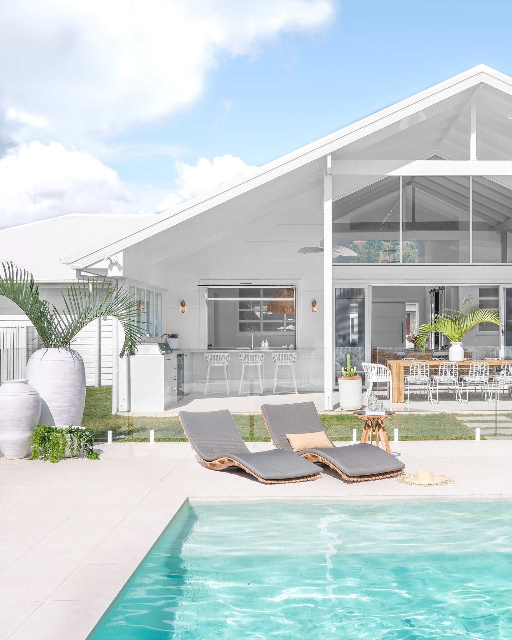 Natural timber Nakuru side table styled poolside beside curved sun loungers, set against a bright white coastal home with open outdoor living and lush greenery.