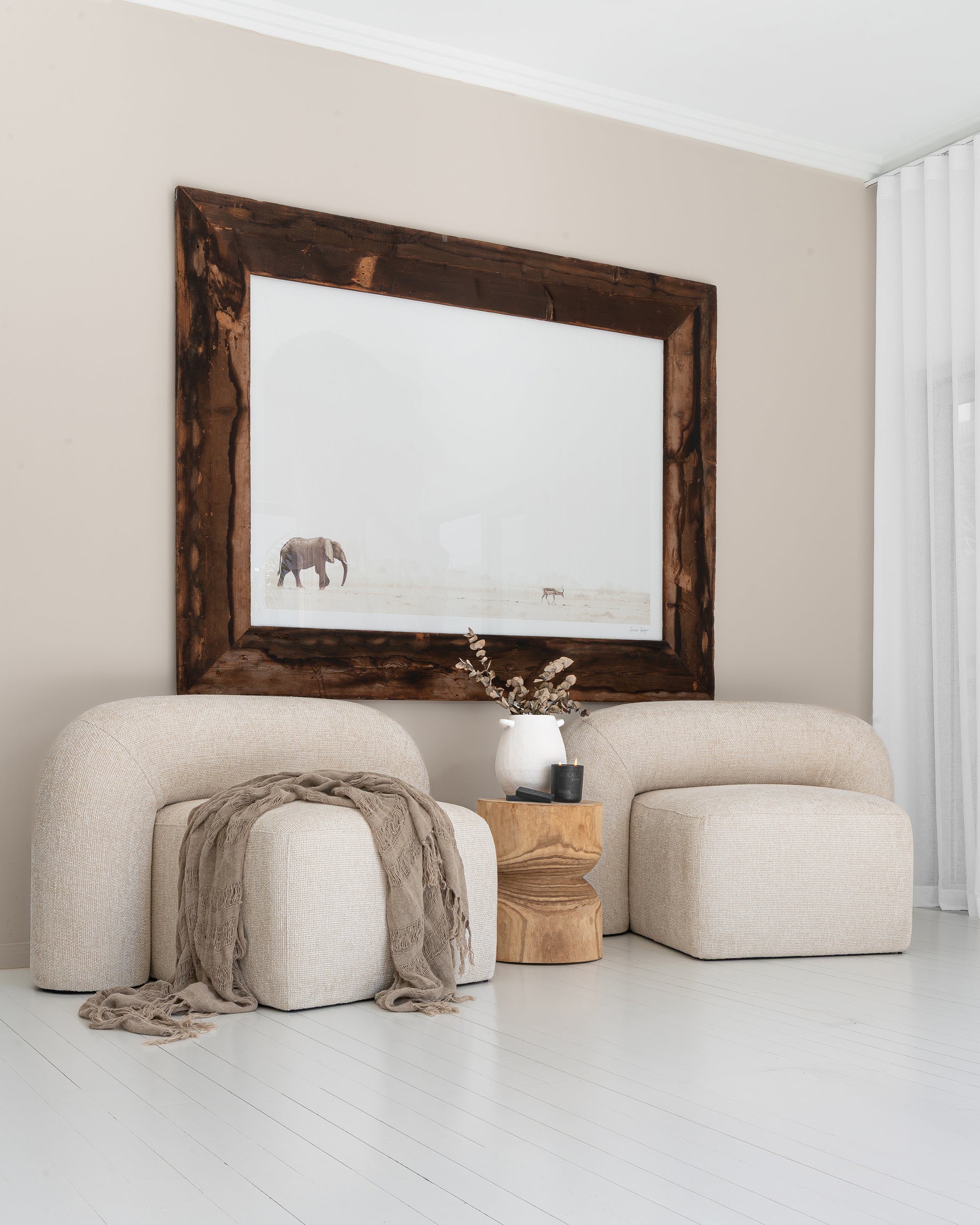 Nash Armchairs in natural upholstery styled with a timber side table, ceramic vase, and elephant wall art in a bright, whitewashed interior