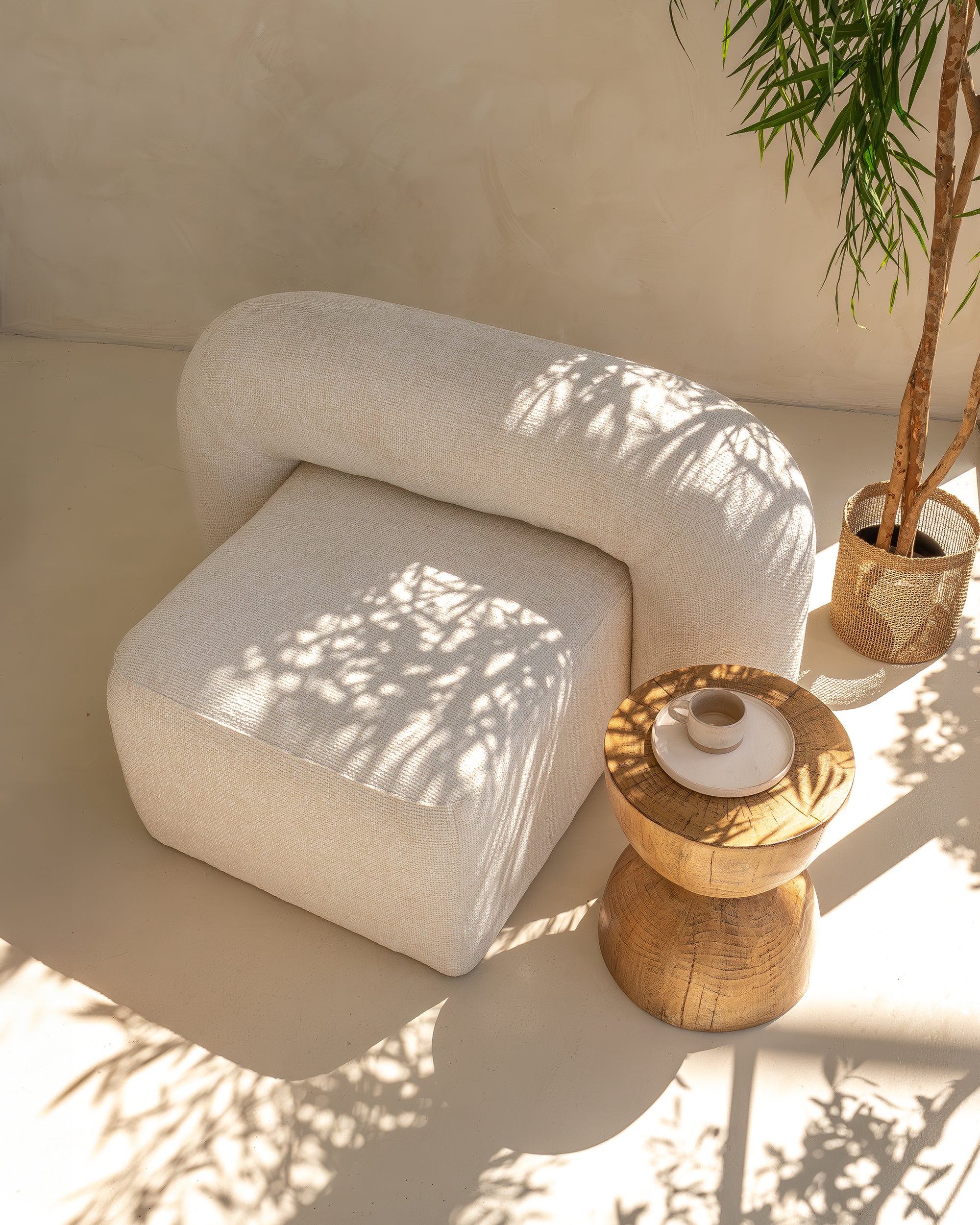 Round coffee table with a textured woodgrain finish, styled with an open book and sculptural brass candlesticks, set between two cream boucle armchairs in a serene, sunlit space