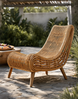 Natural rattan outdoor congo lounger with curved frame styled in a sunny garden setting on stone pavers.