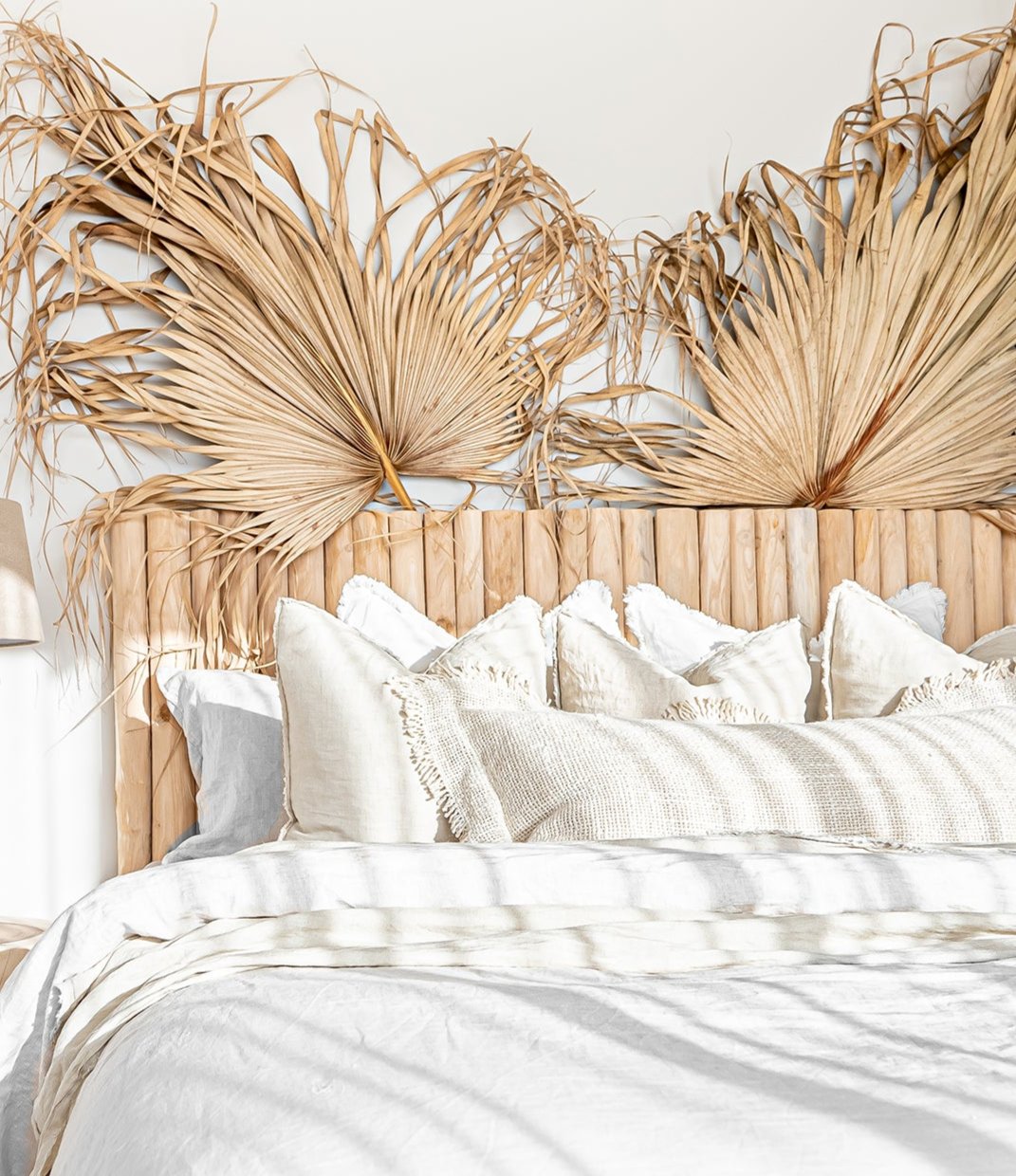 Natural teak wood panel bedhead styled with textured linen bedding and decorative palm leaves. Warm, earthy tones create a serene and inviting bedroom space, blending organic materials with relaxed coastal aesthetics.