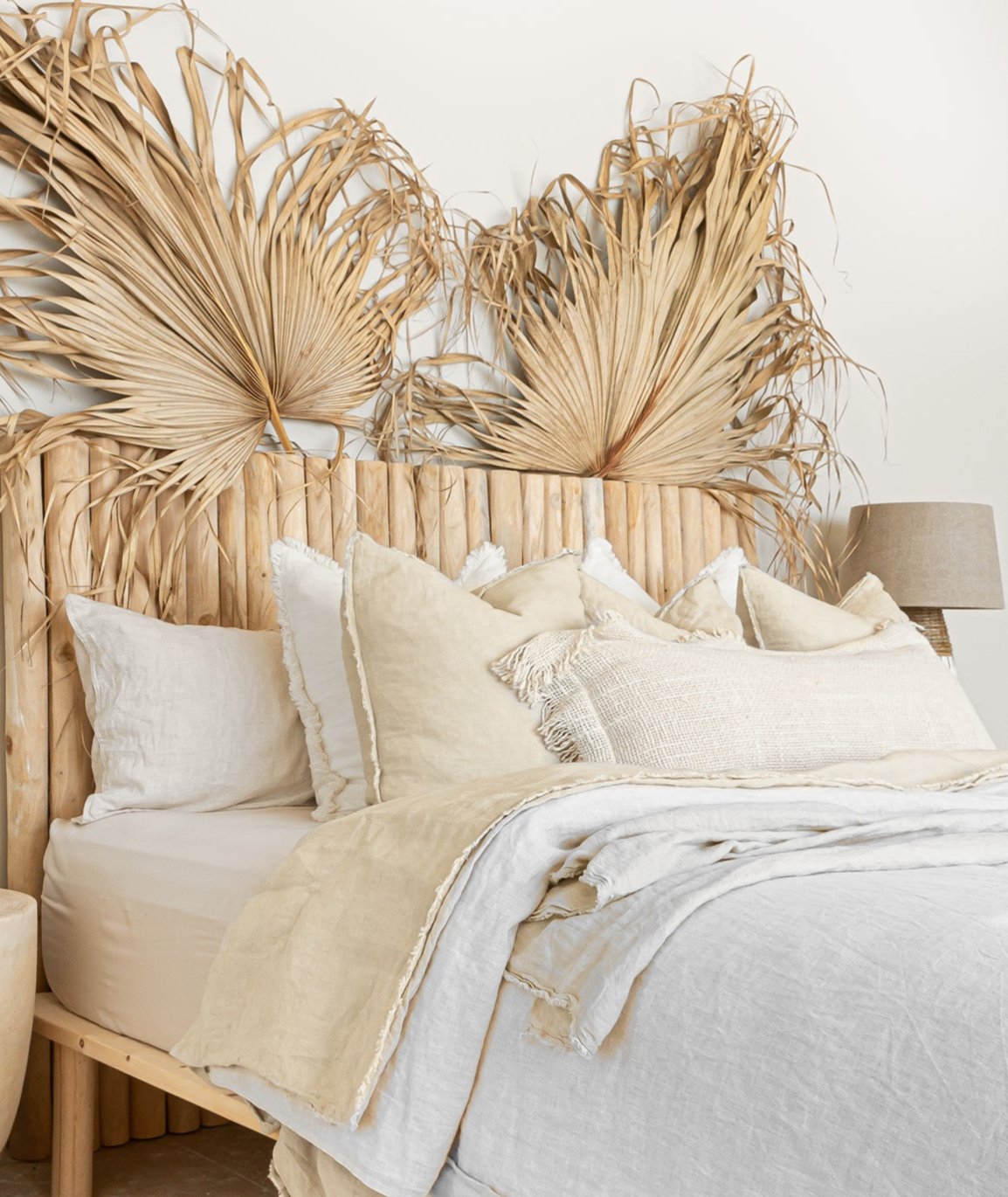 Natural teak wood panel bedhead styled with textured linen bedding and decorative palm leaves. Warm, earthy tones create a serene and inviting bedroom space, blending organic materials with relaxed coastal aesthetics.