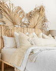 Natural teak wood panel bedhead styled with textured linen bedding and decorative palm leaves. Warm, earthy tones create a serene and inviting bedroom space, blending organic materials with relaxed coastal aesthetics.