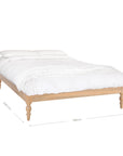 Natural wood platform bed with turned legs styled with white linen bedding and textured throw