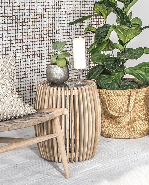 Coastal decor with a natural wooden slatted side table, woven armchair, and indoor plants