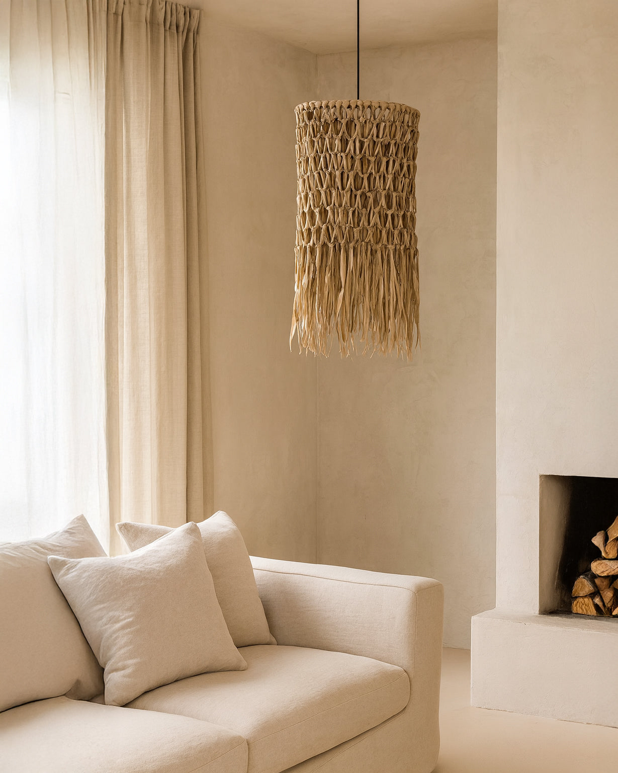 Natural woven pendant light with organic fringe detail hanging above a neutral linen sofa in a soft, minimalist living room