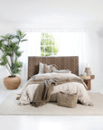 A modern bedroom featuring a woven bedhead with geometric detailing, complemented by soft linen bedding in natural tones, textured cushions, and a neutral woven rug