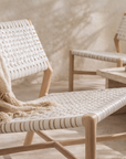 Nayasa occasional chair with woven rope seat and backrest in natural timber, styled in a warm neutral interior with soft throw and stone coffee table.