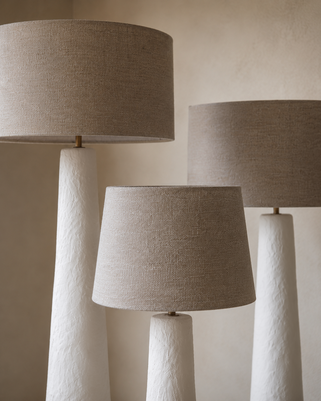 Nhoma lamps in small, medium and large sizes with linen shades styled together in a calm neutral interior, creating layered ambient lighting and sculptural presence.