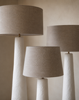 Nhoma lamps in small, medium and large sizes with linen shades styled together in a calm neutral interior, creating layered ambient lighting and sculptural presence.
