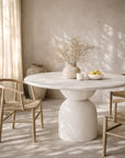 Nuru dining table in eggshell finish with sculptural base styled in a soft sunlit dining room with natural textures and woven chairs.