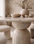 Nuru dining table in stone hydro dipped finish with round top and sculptural pedestal base styled in a soft neutral dining room with textured chairs.