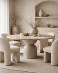 Nuru dining table in stone hydro dipped finish with round top and sculptural pedestal base styled in a soft neutral dining room with textured chairs.