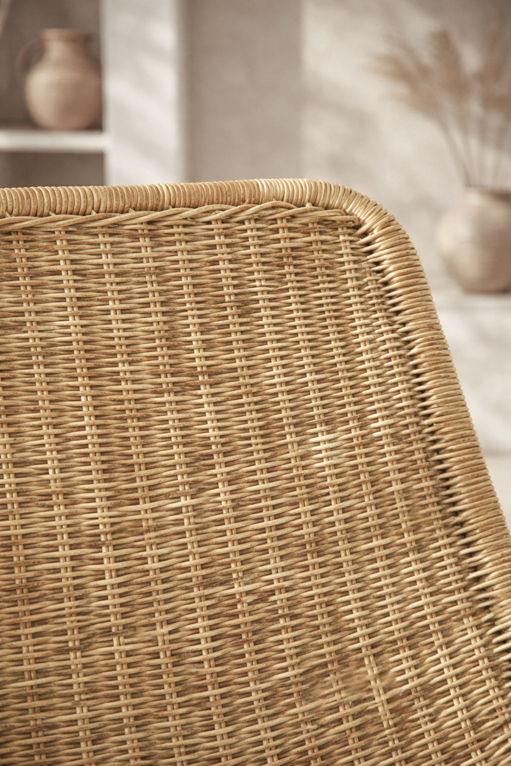 Nyika occasional chair with woven natural rattan seat and backrest on a white metal frame, styled in a warm textured interior.