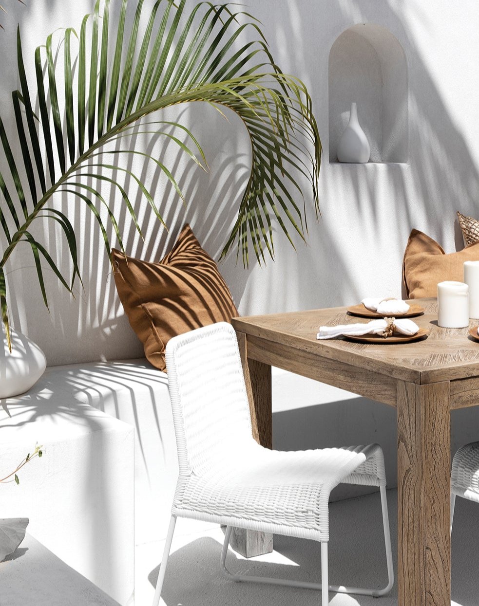 Outdoor dining setting with a white wicker chair and natural wood table, styled with earthy cushions and tropical foliage for a relaxed, coastal vibe.